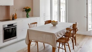 A modern kitchen with white cabinets, a wooden dining table, and hanging pendant lights. - Le Ciel de Marseille , T3 Lumineux Avec une vue Exceptionnelle (Marseille)