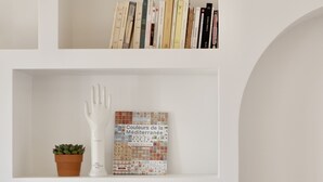 A white shelving unit with books, a white hand-shaped object, a small potted plant, and a brown vase. - Le Ciel de Marseille , T3 Lumineux Avec une vue Exceptionnelle (Marseille)