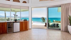 A spacious kitchen with a view of the ocean, a sliding glass door leading to a balcony, and a ceiling with decorative wooden elements. - Luxury Beachfront Gem ~ Panoramic Sea Views ~ Heated Pool (B.C.S.)