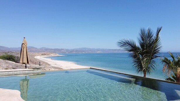 A clear blue pool with a view of a beach and mountains. - Luxury Beachfront Gem ~ Panoramic Sea Views ~ Heated Pool (B.C.S.)