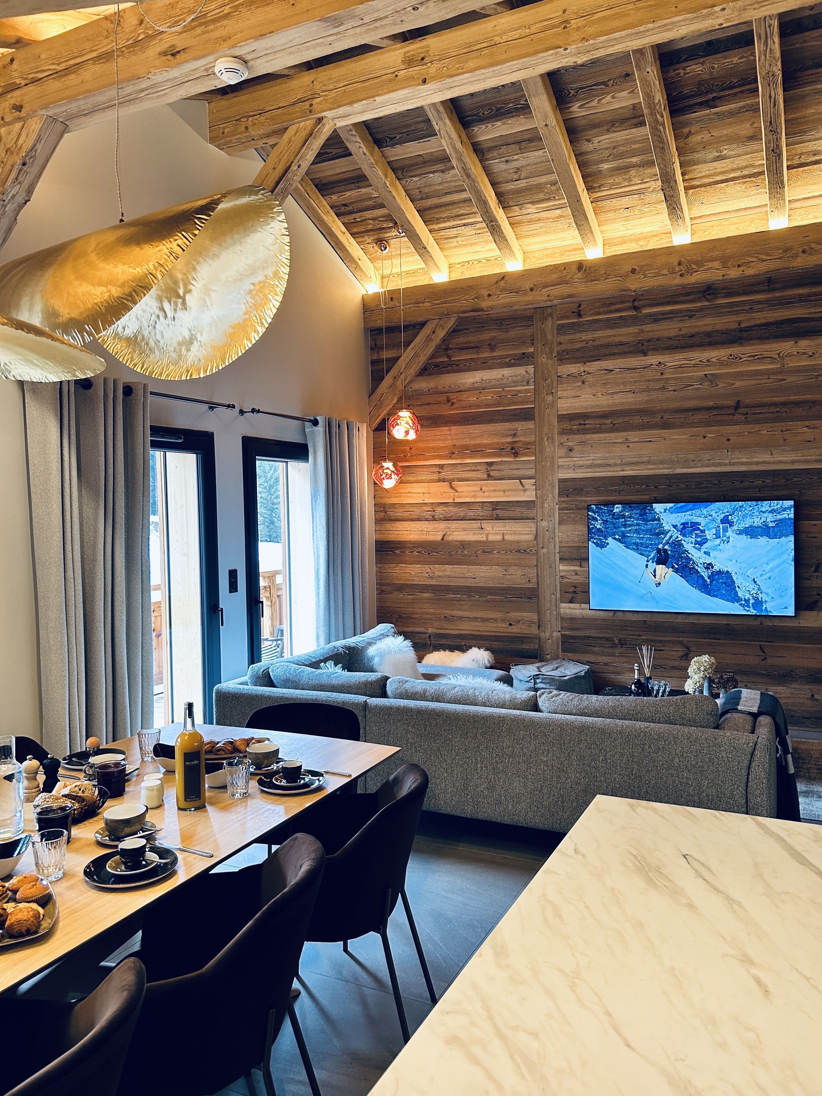 Un salon chaleureux avec un plafond en bois, un grand téléviseur à écran plat, un canapé et un coin repas avec une table mise pour le repas.