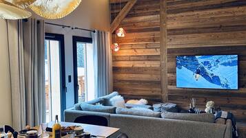 Un salon chaleureux avec un plafond en bois, un grand téléviseur à écran plat, un canapé et un coin repas avec une table mise pour le repas.