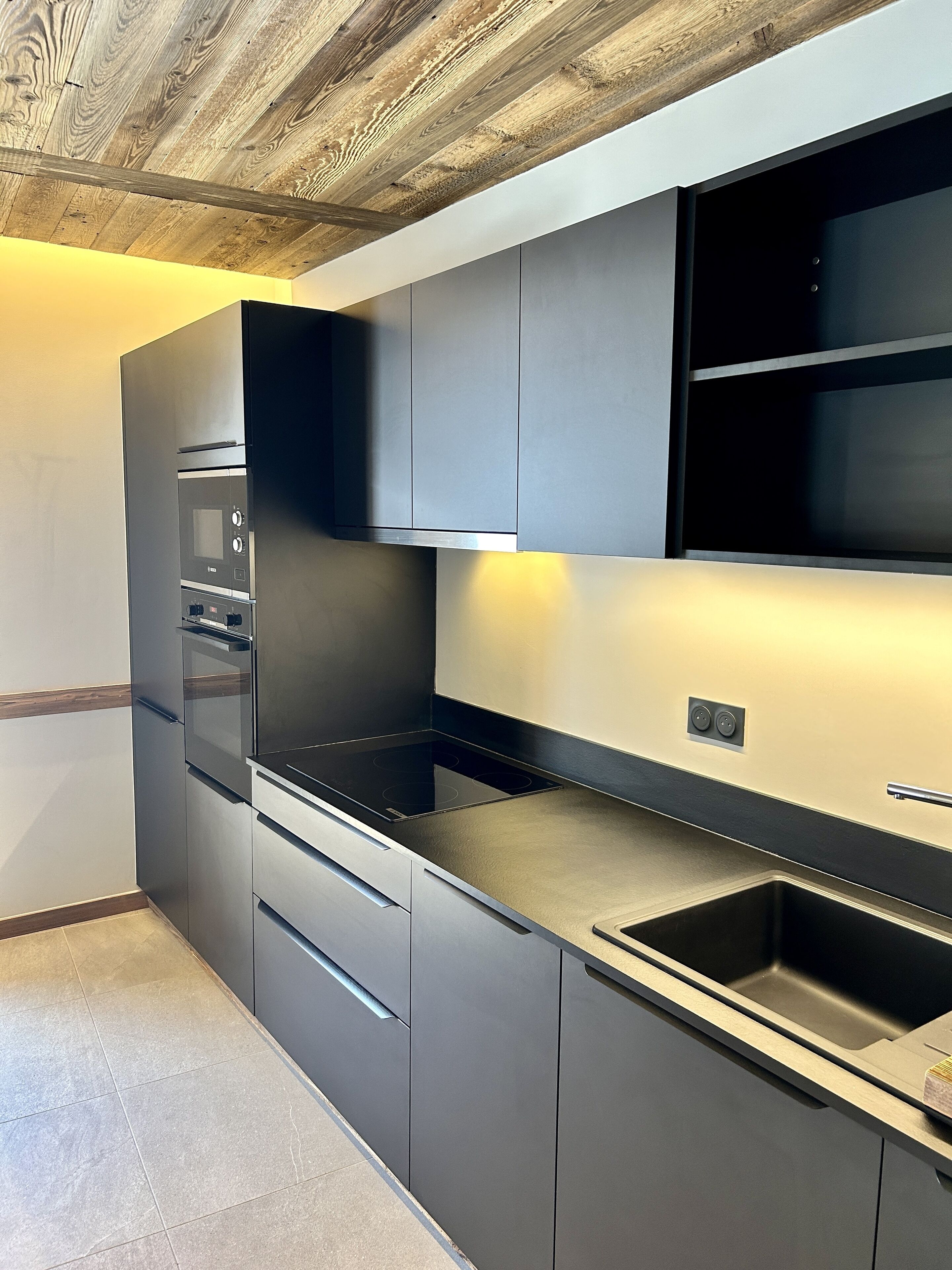 Une cuisine moderne dotée d’appareils électroménagers intégrés, de meubles de rangement gris et d’un plafond en bois.