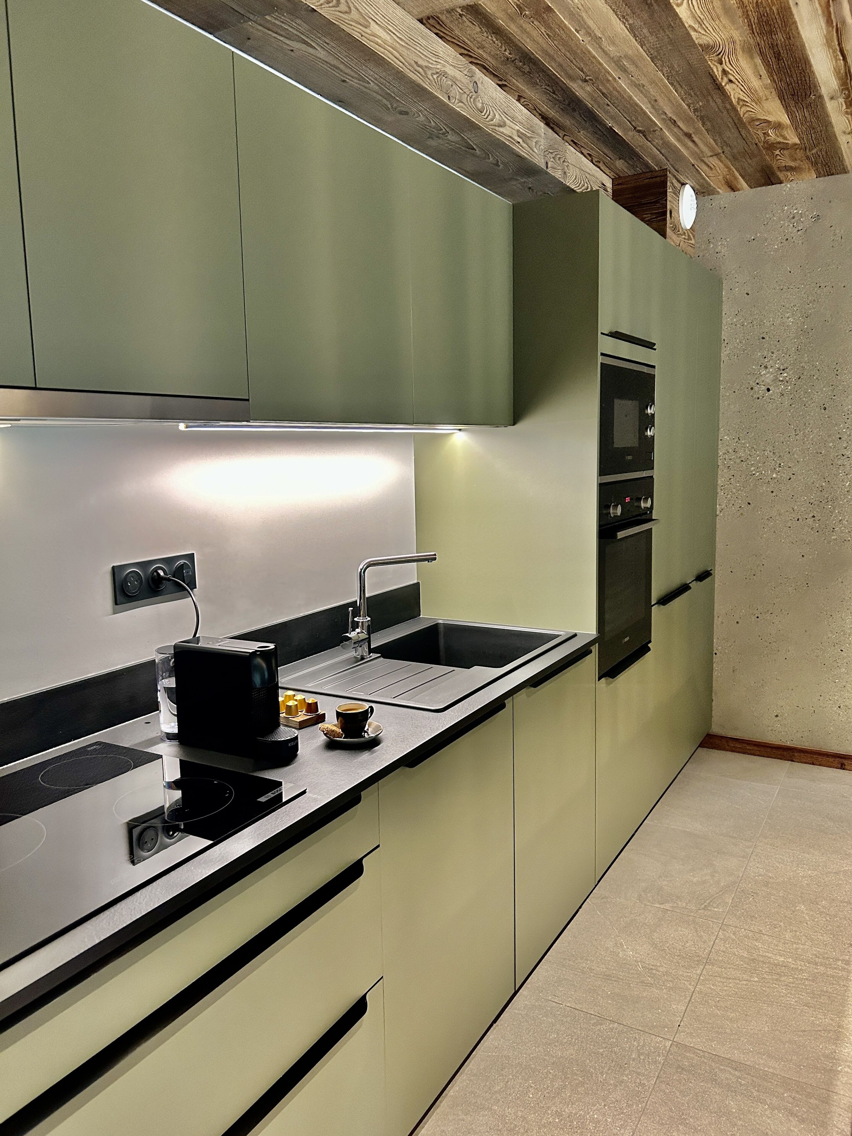 A modern kitchen with a built-in oven, a sink, and a countertop with a coffee maker and a glass of water.