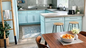 A modern kitchen with light blue cabinets, a wooden dining table, and a large window with a view. - Naples Art District (Naples)