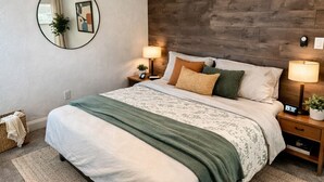 A bedroom with a bed, a round mirror, two bedside tables with lamps, a ceiling fan, and a wooden accent wall. - Naples Art District (Naples)