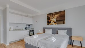 A modern bedroom with a large bed, a small kitchen area, and a painting on the wall. - Villa Winter Apt. 2 (Funchal)