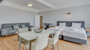 A modern hotel room with a grey sofa, a dining table with chairs, and a bed with white bedding. - Villa Winter Apt. 2 (Funchal)
