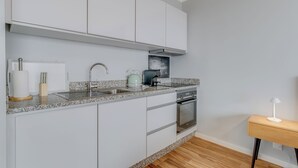 A modern kitchen with white cabinets, a granite countertop, a kettle, a toaster, and a small wooden table with a lamp. - Villa Winter Apt. 2 (Funchal)