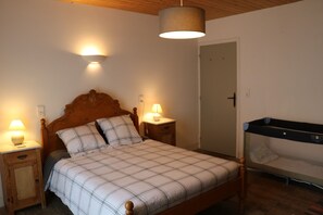 A bedroom with a wooden bed, two bedside tables with lamps, a hanging light fixture, and a door to another room.