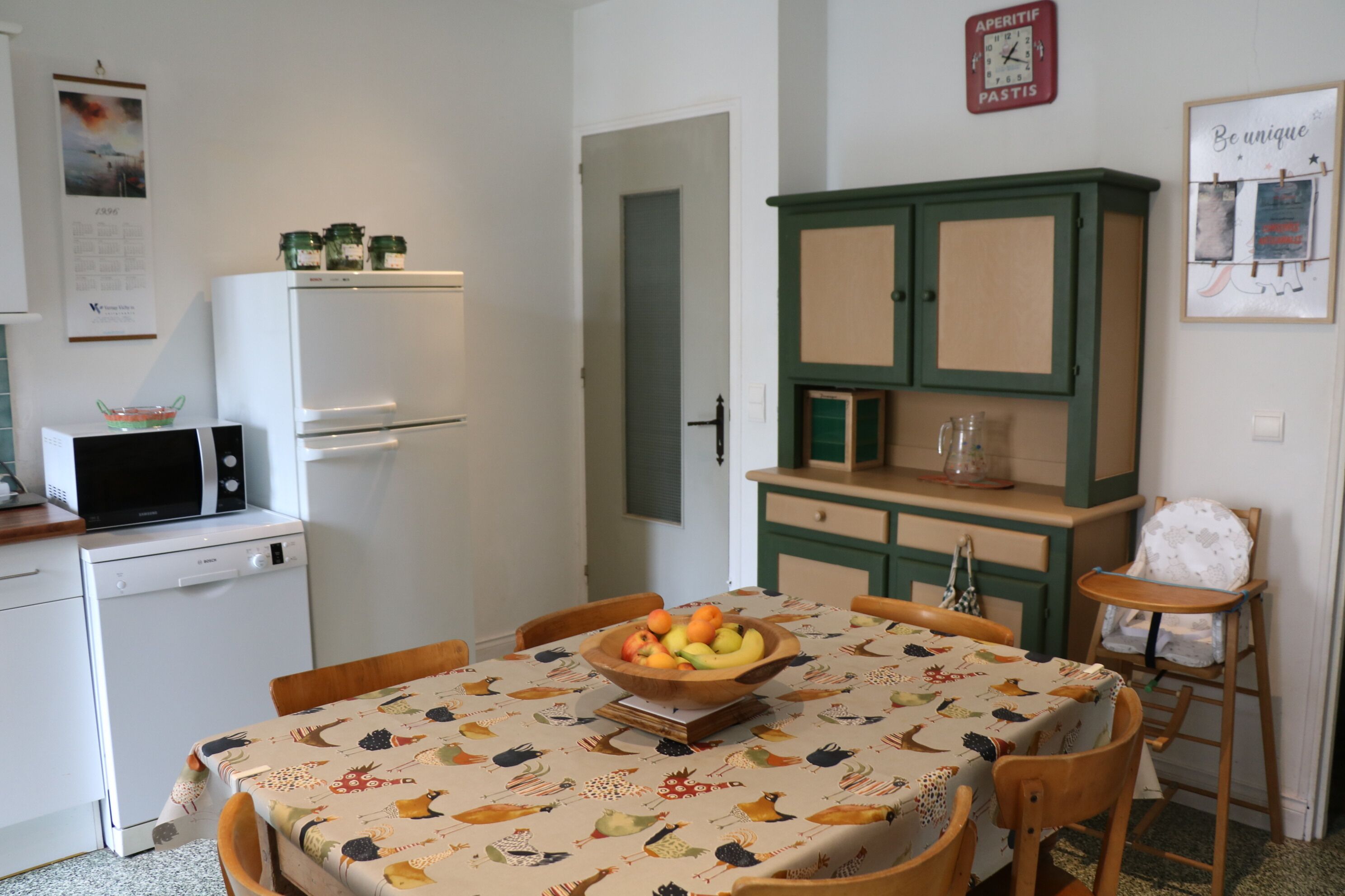 Eine kleine Küche mit einem Tisch für zwei Personen, einer Mikrowelle, einem Kühlschrank und einem Schrank mit einer Uhr.