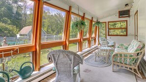 A sunlit room with large windows, wicker furniture, and a view of a fenced yard.