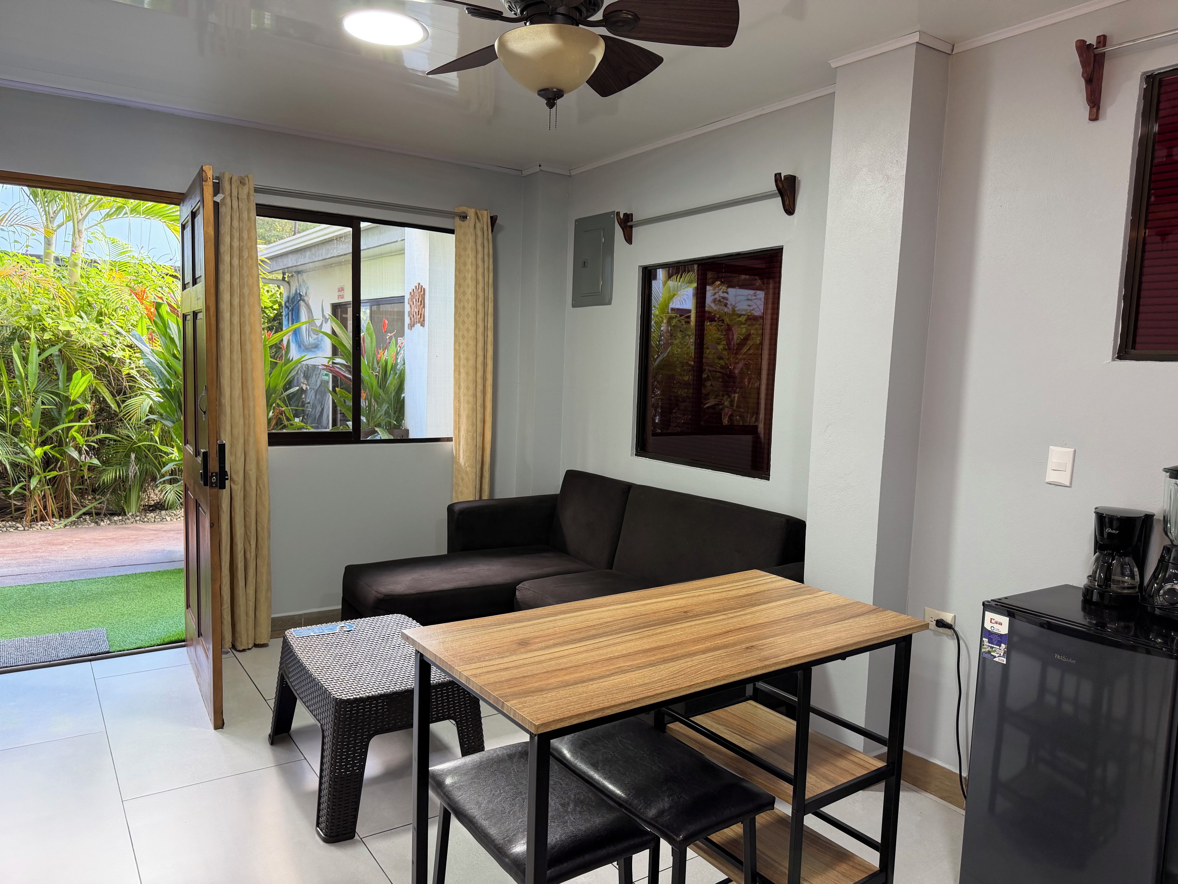 A compact room with a ceiling fan, a sofa, a small table, and a refrigerator.