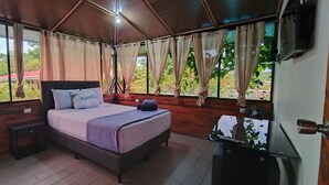 A bedroom with a bed, wooden walls, a window with curtains, a bedside table, and a TV. - Hotel Ballena REY (Bahía Ballena)