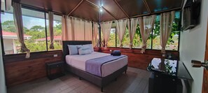 Een slaapkamer met een bed, houten wanden, een raam met gordijnen, een nachtkastje en een televisie.
