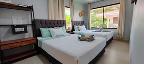 Een hotelkamer met twee bedden, een houten nachtkastje, een in de muur gemonteerde kluis en een raam met uitzicht op groen.