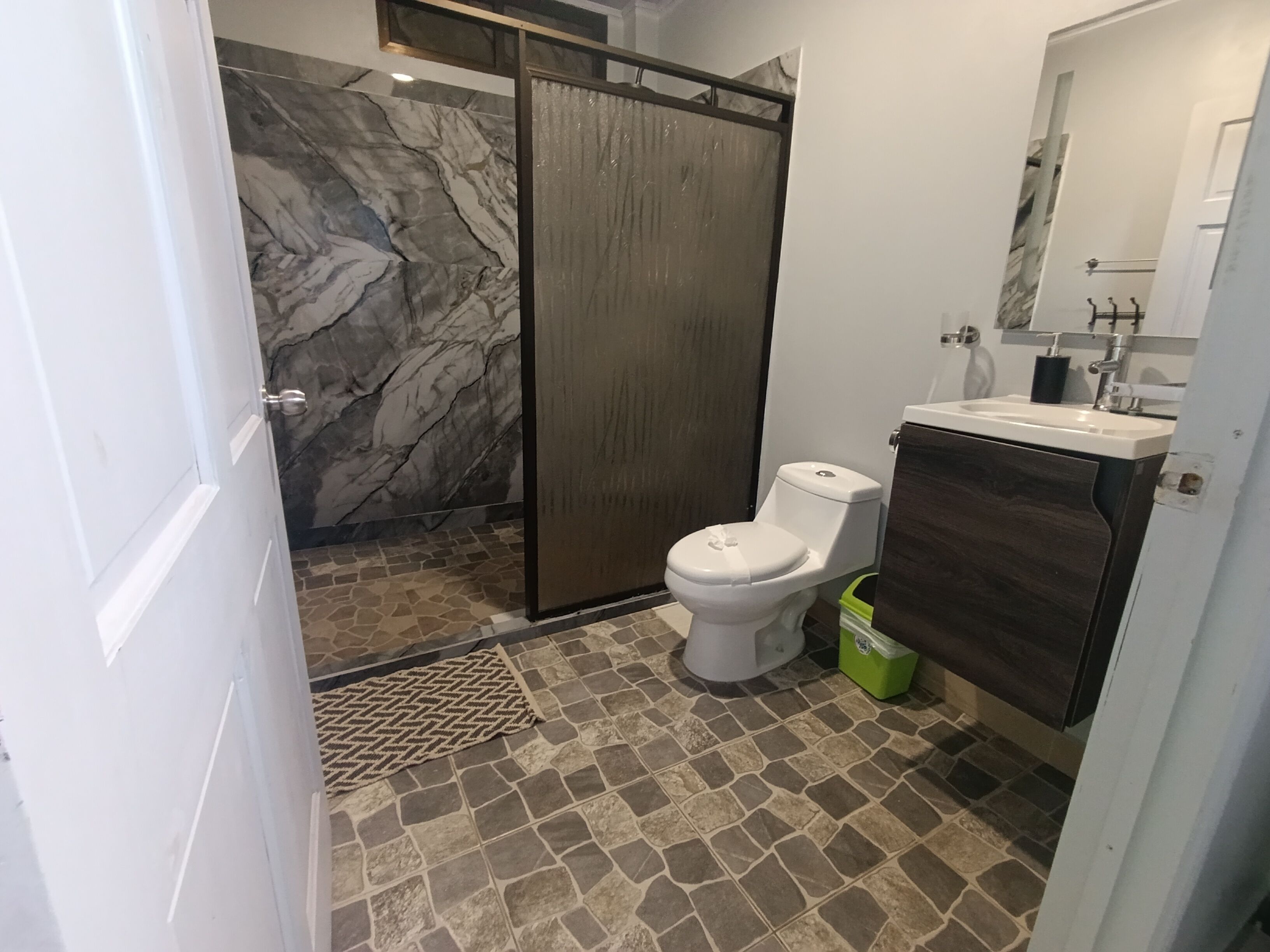 A bathroom with a marble wall, a toilet, a sink, and a shower area.