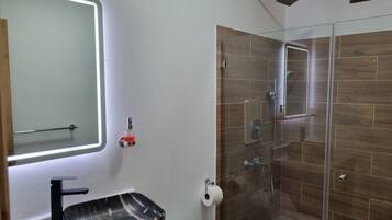 Un baño con ducha acristalada, lavamanos de mármol negro y espejo con luz integrada.
