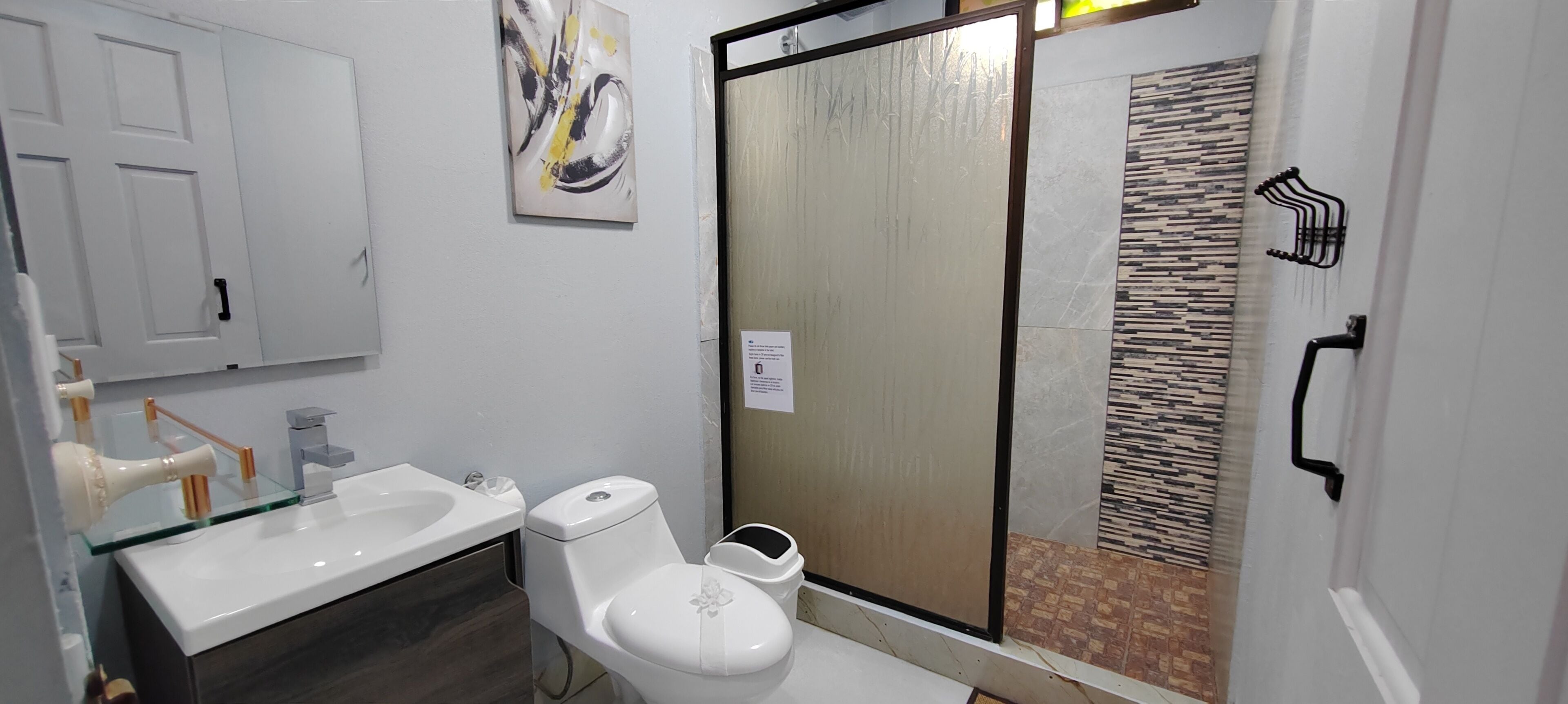 A bathroom with a glass shower enclosure, a white toilet, a glass sink, and a mirror.
