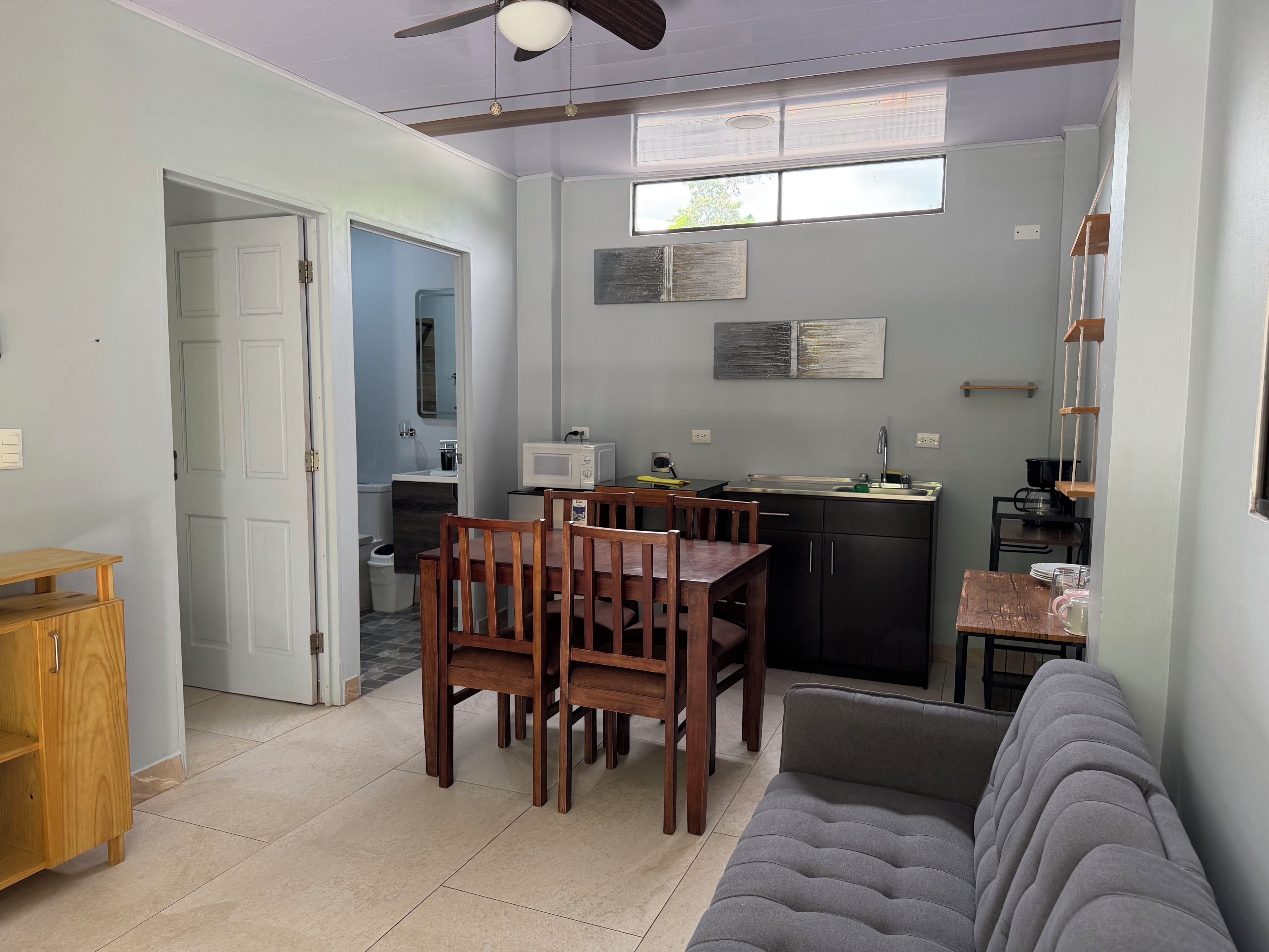 Un espacio habitable compacto con comedor, kitchenette y un sofá gris.
