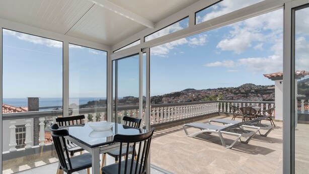 A balcony with a table and chairs, a view of the sea and a town, and a tiled floor. - Villa Winter Apt. 3 (Funchal)