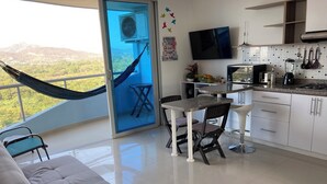 A modern kitchen with a dining area, a sofa, and a view of the mountains through a glass door.
