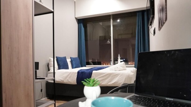 Ett modernt hotellrum med en säng, en bärbar dator på ett bord och utsikt över staden genom fönstret.