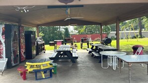 A covered picnic area with tables and benches, a ceiling fan, and a Coca-Cola mural. - Sportsman's Lodge (Higden)