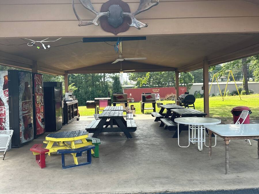 Un área de picnic techada con mesas y bancos, un ventilador de techo y un mural de Coca-Cola.