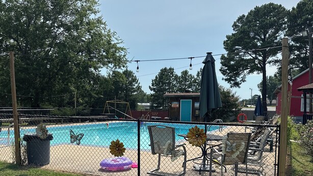 A fenced backyard with a swimming pool, lounge chairs, and a patio area. - Sportsman's Lodge (Higden)