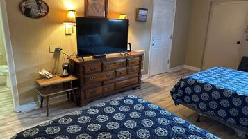 Ein Zimmer mit zwei Betten, einem Fernseher auf einer Kommode, einer Kaffeemaschine und einem Willkommensschild.