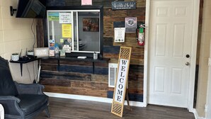 A reception area with a wooden wall, a 'WELCOME' sign, a TV mounted on the wall, and a door to the right. - Sportsman's Lodge (Higden)