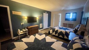 A bedroom with two beds, a dresser, a TV, and a sign on the wall. - Sportsman's Lodge (Higden)