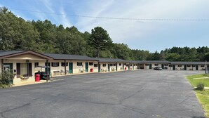 A motel with multiple rooms, a parking lot, and a covered outdoor seating area. - Sportsman's Lodge (Higden)