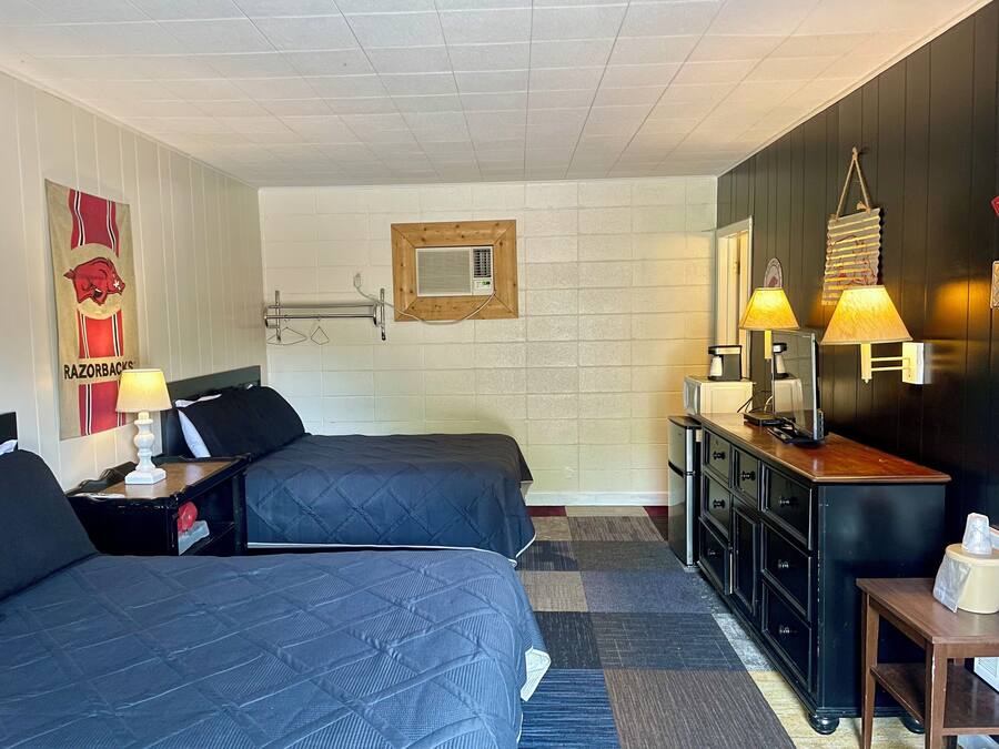 Habitación de hotel con dos camas, un aparador de madera, un espejo y una lámpara de pared.