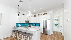 A modern kitchen with white cabinets, a central island with bar stools, stainless steel appliances, and a blue backsplash. - Steps To Beach & Lagoon, Overlooks Pool, Balcony Gulf Views, 4BR House, Sleep 12 (Gulf Shores)