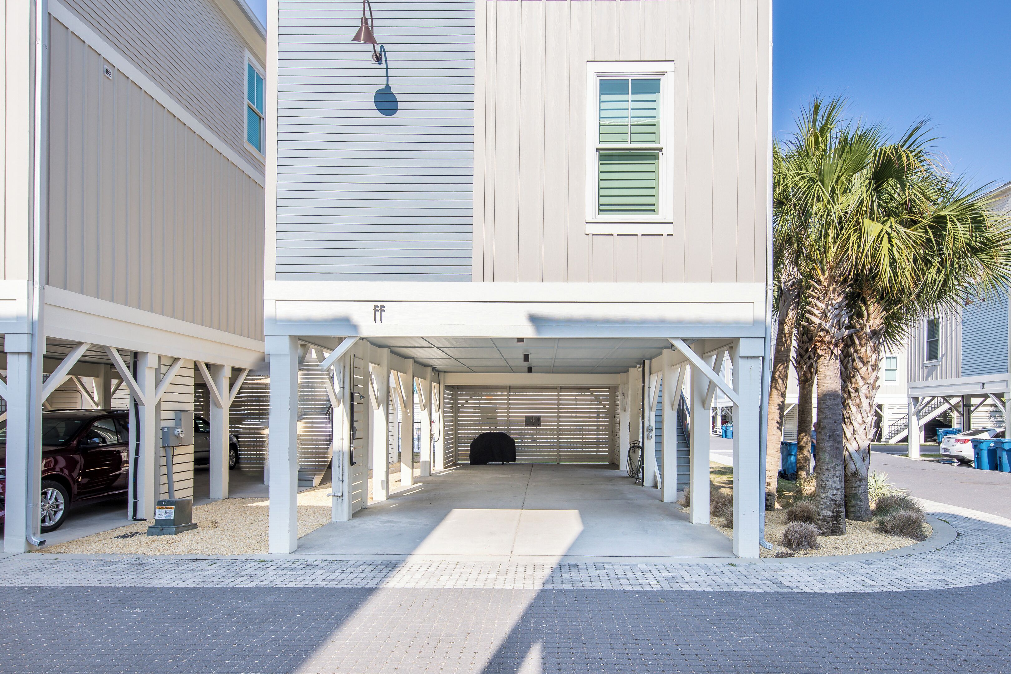 A covered parking area with a garage door, a covered walkway, and a palm tree.