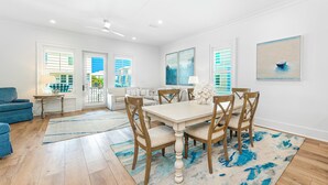 A spacious living room with a dining area, wooden flooring, and large windows. - Steps To Beach & Lagoon, Overlooks Pool, Balcony Gulf Views, 4BR House, Sleep 12 (Gulf Shores)