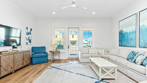 A modern living room with a blue armchair, a white sofa, a wooden coffee table, and a large window with blinds. - Steps To Beach & Lagoon, Overlooks Pool, Balcony Gulf Views, 4BR House, Sleep 12 (Gulf Shores)