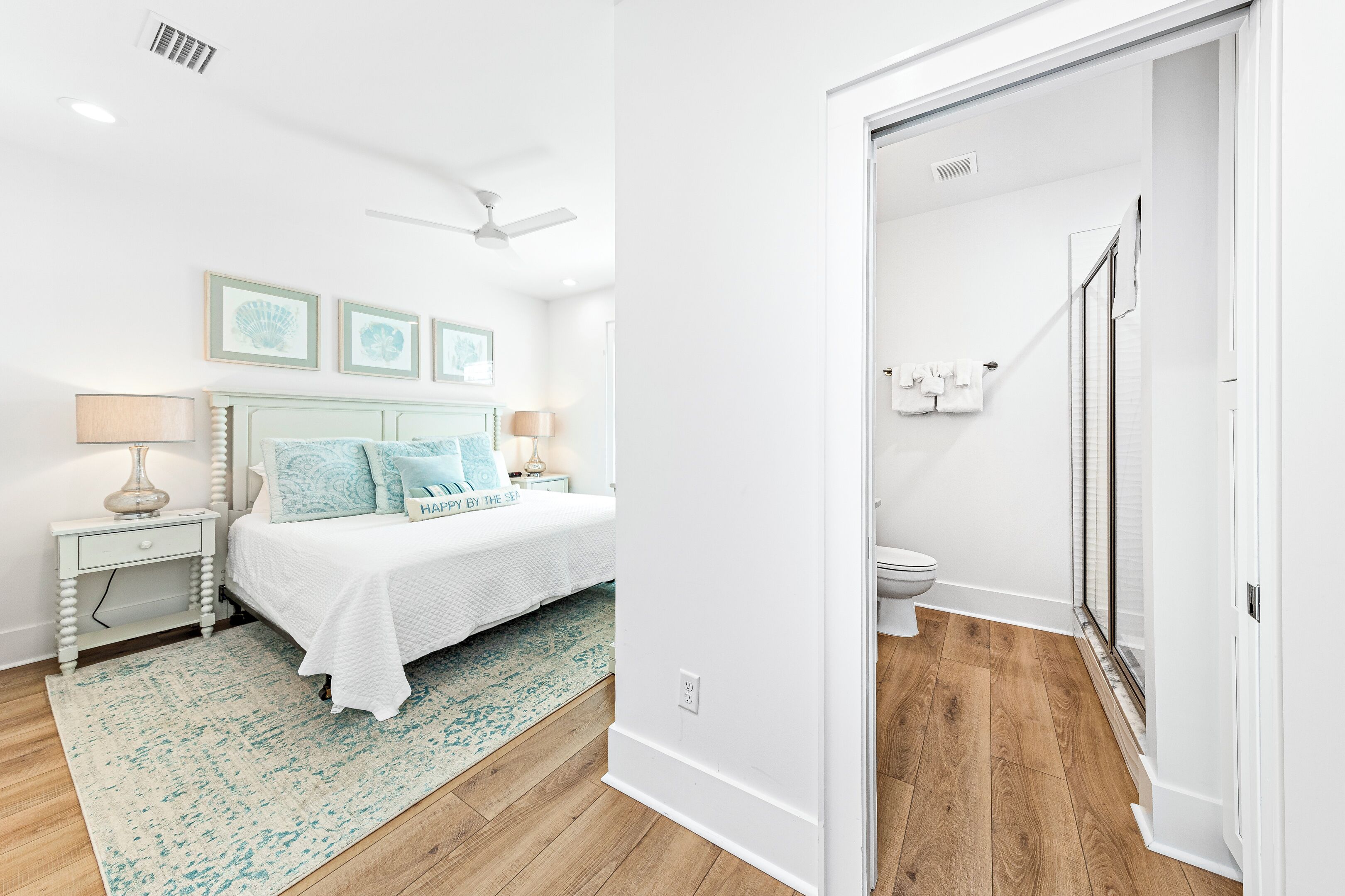 A bedroom with a bed, bedside tables, a ceiling fan, and a bathroom with a toilet and shower.