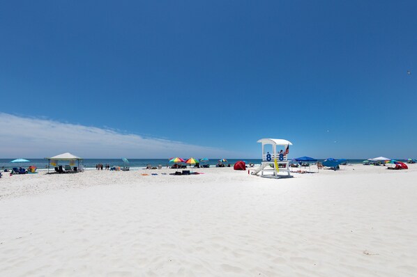A beach with a lifeguard tower, umbrellas, and beach chairs.