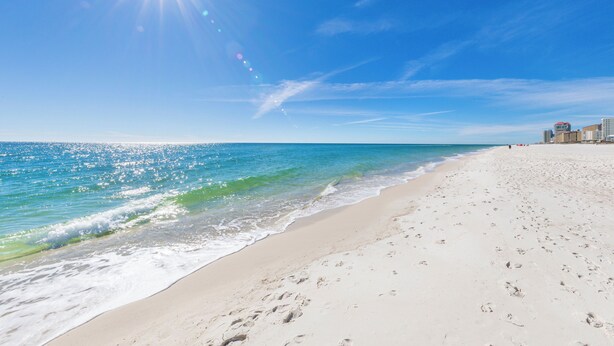 A beach with footprints leading to the water, a clear sky, and buildings in the background. - Steps To Beach & Lagoon, Overlooks Pool, Balcony Gulf Views, 4BR House, Sleep 12 (Gulf Shores)