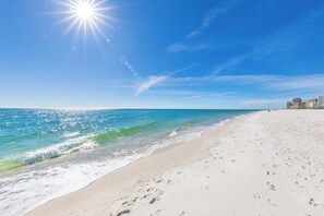 A beach with footprints leading to the water, a clear sky, and buildings in the background. - Steps To Beach & Lagoon, Overlooks Pool, Balcony Gulf Views, 4BR House, Sleep 12 (Gulf Shores)