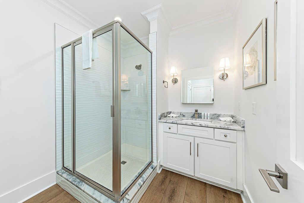 Un baño moderno con ducha envuelta en vidrio, muebles blancos y encimeras de mármol.