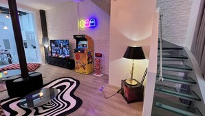 Een moderne woonkamer met een flatscreen televisie, speelautomaten, een vloerkleed met zebrapatroon en een trap.