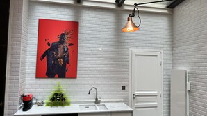 Een moderne badkamer met een witte baksteenmuur, een witte deur, een wastafel met kraan, een groene fleshouder en een rode kunstwerk.