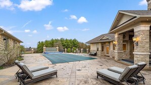 Un patio con dos sillones, una piscina y un edificio de piedra con terraza cubierta.