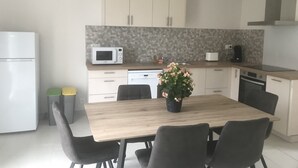 Une cuisine moderne avec une table à manger en bois, des chaises grises, un four à micro-ondes, un lave-vaisselle et une plante en pot.
