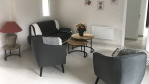 Un salon moderne avec un canapé noir et blanc, une petite table ronde ornée d’un pot de plante, une lampe rouge et un plaid à motifs.
