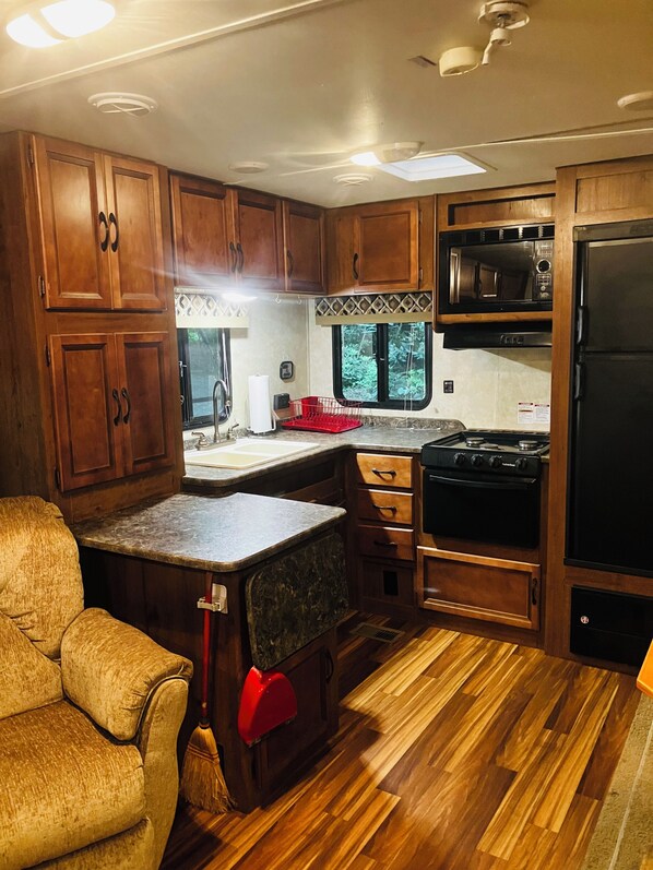 A compact RV kitchen with wooden cabinets, a stove, a microwave, and a refrigerator. - Serenity now (Fancy Gap)